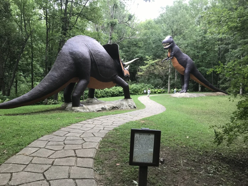 Two large dinosaur statues flanking the stone trail at Prehistoric World, with informational plaques