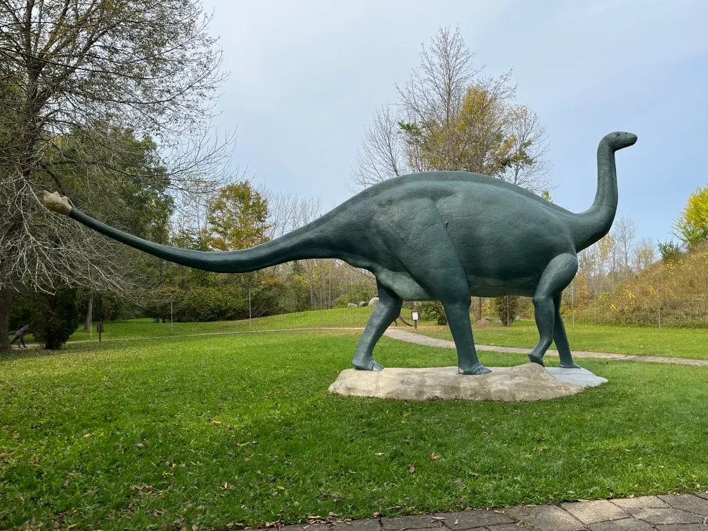 A large green Brontosaurus statue in an open grassy clearing