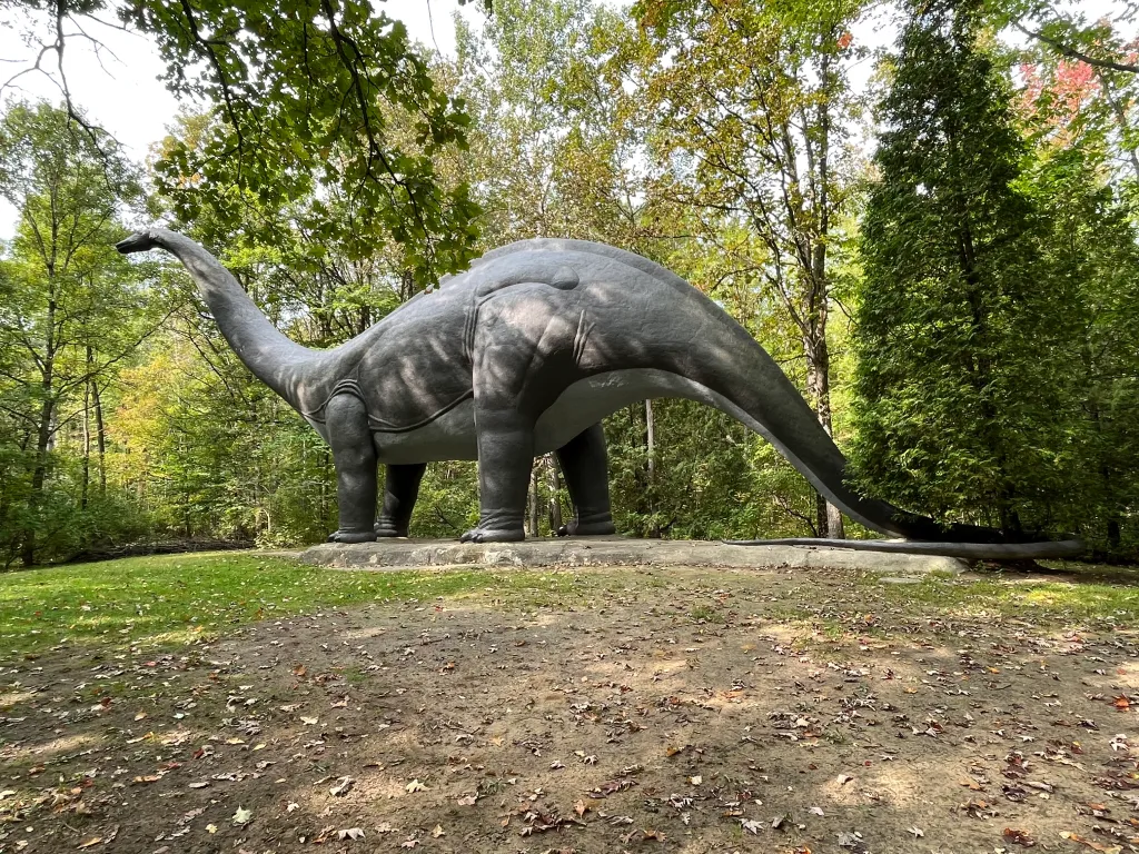 A massive grey Brontosaurus statue in a forest clearing
